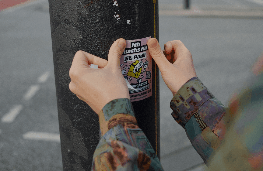 Hände kleben einen Kampagnen-Sticker auf einen Laternenpfahl